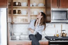 a woman sitting on the kitchen counter with dishes in front of her and she is looking up