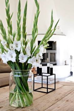 a glass vase filled with white flowers sitting on top of a wooden table next to a couch