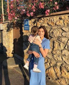 a woman holding a child in front of a stone wall with pink flowers on it