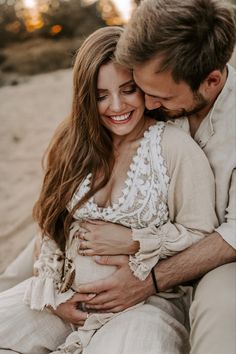 a man and woman cuddling on the beach at sunset with their arms around each other