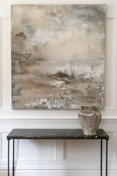 an abstract painting hangs on the wall above a black table with a white vase sitting on it