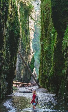 a woman wading through a river surrounded by mossy cliffs