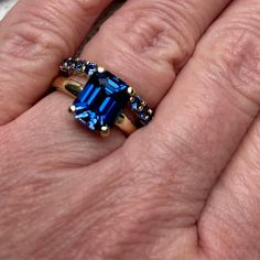 a woman's hand holding a blue ring with two different colored stones on it