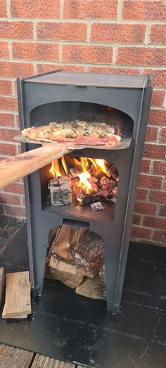 the pizza is being cooked in an outdoor wood burning oven with firewood and logs