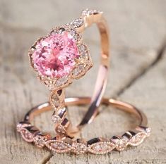 two gold rings with pink and white diamonds on them sitting on a piece of wood