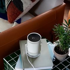 a white speaker sitting on top of a table next to a potted green plant