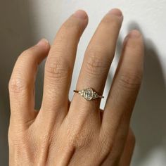 a woman's hand with a diamond ring on top of her left hand, against a white wall