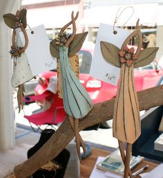 three wooden angel ornaments hanging from a tree branch in front of a table with other items on it