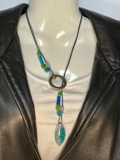 Brilliant Turquoise Dragon's Vein Agate pendant in Lariat or "Y" style necklace. Chrysocolla, Blue Sky Agate, Peridot Agate, Blue Stripe Agate, and Silver Alloy on two strands of leather. A 2mm Gunmetal Gray, and a 1mm Silver cord. Necklace is 22" long, pendant is 1 1/2" x 3/4" and alloy ring is 1 1/4" around. Small Vortex char can be deleted or removed. To wear place open necklace around neck, then put pendant thru ring and adjust as you wish. No lead or nickel used. Please use the Last On, First Off approach. Stones discolor with lotions, perfumes, hairspray, sweat, chlorine, even some soaps, and will break if dropped. Adjustable Multicolor Lariat Necklace With Colorful Beads, Adjustable Green Lariat Necklace, Artisan Turquoise Lariat Necklace Adjustable, Artisan Turquoise Adjustable Lariat Necklace, Colorful Beads Lariat Necklace Gift, Artisan Adjustable Turquoise Lariat Necklace, Colorful Beads Lariat Necklace For Gift, Adjustable Multicolor Beaded Lariat Necklace, Adjustable Lariat Necklace With Colorful Beads For Gift