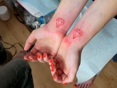 two people holding hands with tattoos on their arms and fingers, both showing red ink