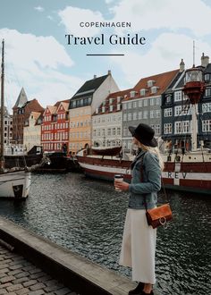 a woman standing on a dock next to boats in the water and buildings behind her