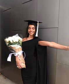 a woman in a graduation cap and gown holding flowers, with her arms outstretched out