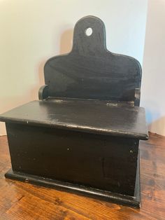 an old black wooden box with a handle on the top sitting on a hard wood floor