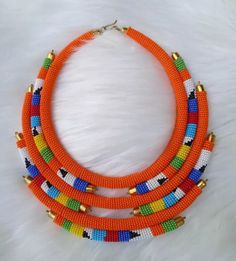 Do you intend to be creative in your dressing code and tobe unique and at the same time standout as fashionable? Then look no more, We Do you have intention to be creative in your dressing code and tobe unique and at the same time standout as fashionable? Then look no more, We African 1 Stores brings to you the most colorful necklace to supplement your style and fashion.  Can be won on almost all occasions which includes Beach travels, Outdoor walks and adventures, Party and ceremonies. Designed Unique Orange Beaded Necklace With Colorful Beads, Unique Orange Beaded Necklace, Orange Choker With Colorful Beads, Handmade Orange Beaded Choker Necklace, Unique Colorful Beads Choker, Unique Beaded Necklaces With Gold Beads, Unique Beaded Necklace With Gold Beads, Orange Beads As A Gift, Unique Gold Beaded Necklaces With Round Beads