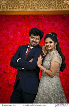 a man and woman standing next to each other in front of a red flower wall