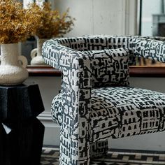 a black and white patterned chair sitting in front of a table with vases on it