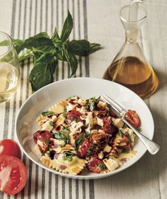 a white bowl filled with pasta and vegetables next to a bottle of olive oil on a table