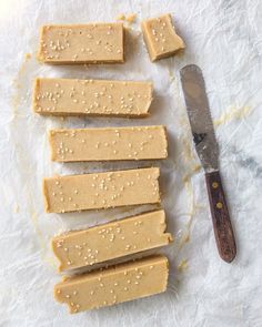 five pieces of peanut butter next to a knife on a piece of wax paper with sesame seeds