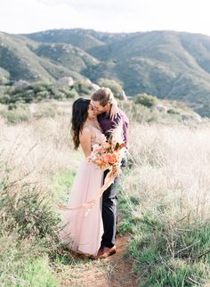 a bride and groom kissing on the side of a dirt road with mountains in the background