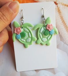 These cute Sea Turtle Earrings are handmade from polymer clay, resulting in a unique and eye-catching accessory. The earrings feature a beautifully painted shell design with delicate floral and succulent decorations in a mixture of pastel colours. Measuring approximately 3 cm in length, these earrings are the perfect size to make a statement. Despite their detailed design, they are remarkably lightweight, ensuring comfortable wear throughout the day. To add a touch of elegance and durability, ea Playful Hand Painted Resin Jewelry, Handmade Playful Resin Jewelry, Cute Multicolor Polymer Clay Jewelry, Playful Green Polymer Clay Jewelry, Playful Polymer Clay Jewelry For Gifts, Playful Polymer Clay Jewelry As A Gift, Cute Handmade Green Jewelry, Cute Resin Jewelry With Matching Earrings, Cute Green Hand Painted Jewelry