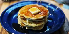 a blue plate topped with pancakes covered in butter and syrup on top of a wooden table