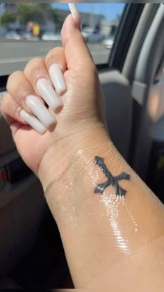 a woman's arm with white nails and a cross tattoo on her left wrist