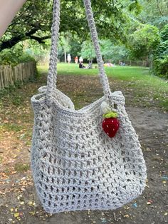 a crocheted bag with a strawberry on it hanging from a tree in the park