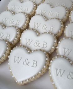 heart shaped cookies with white frosting and monogrammed letters are arranged on a platter