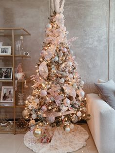 a white christmas tree with pink and silver ornaments in a living room next to a couch