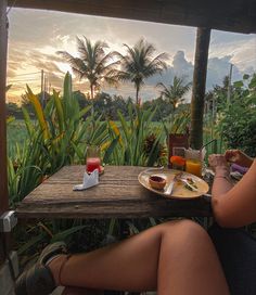 a woman sitting at a table with food and drinks in front of her on the porch