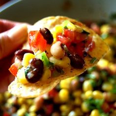 a hand holding a tortilla filled with beans, corn and tomato salsa on it