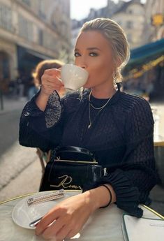 a woman sitting at a table drinking from a cup