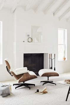 an eames lounge chair and ottoman in a living room with white carpet, fireplace and windows