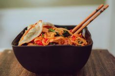 a bowl filled with noodles, meat and vegetables next to chopsticks on a wooden table