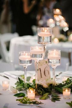 a table topped with lots of candles next to glasses filled with water and greenery