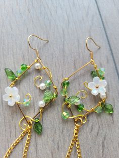 two pairs of earrings with green and white flowers on them sitting on a wooden surface