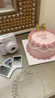 a pink birthday cake sitting on top of a table next to a camera and polaroid