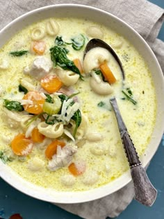 a white bowl filled with pasta and veggies next to a spoon on top of a napkin