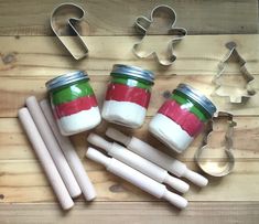 four jars with red, green and white frosting on them next to cookie cutters