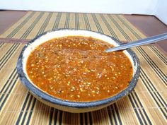 a bowl filled with chili sauce on top of a striped table cloth next to a spoon