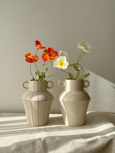 two vases with flowers in them sitting on a tableclothed surface, next to each other