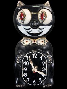 a black and white cat clock with red eyes on it's face, sitting in front of a black background