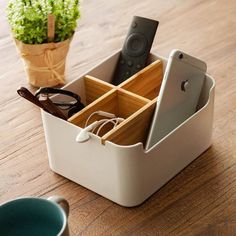 a table with a cup, glasses and remote control in it next to a potted plant