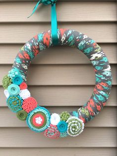 a colorful wreath hanging on the side of a house with buttons and yarn around it