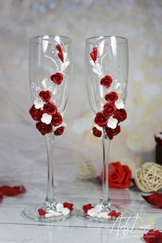 two wine glasses decorated with red roses and white petals, sitting on a wooden table