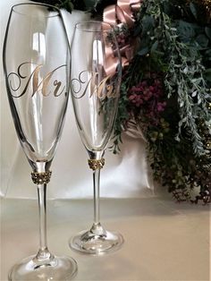 two wine glasses with the word merry written on them next to greenery and a pink ribbon