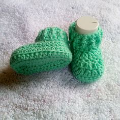 two green crocheted slippers sitting on top of a white carpet next to a bottle