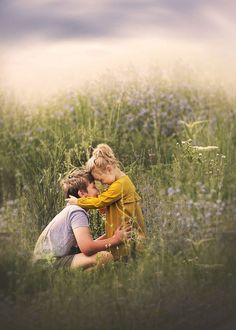 two people sitting in the middle of a field with blue flowers on it and one person hugging