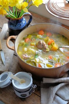 a pot filled with soup sitting on top of a wooden table next to a cup