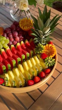 a bowl filled with sliced up fruit on top of a wooden table next to flowers